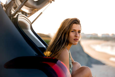 Beautiful woman sitting in the trunk of a car and looking to the sea