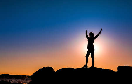 Beautiful woman at the beach on top a of a rock in silhouetteの写真素材