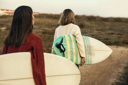 Two female surfers walking near the coastline with surfboardsの写真素材