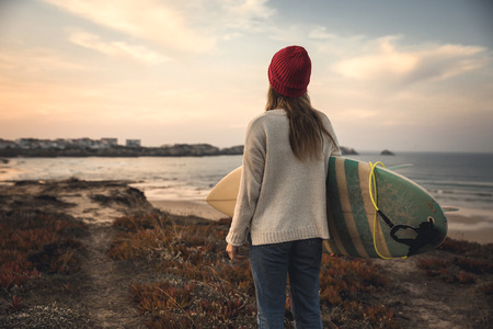 Surfer girl near the coastline with her surfboard searching for wavesの写真素材