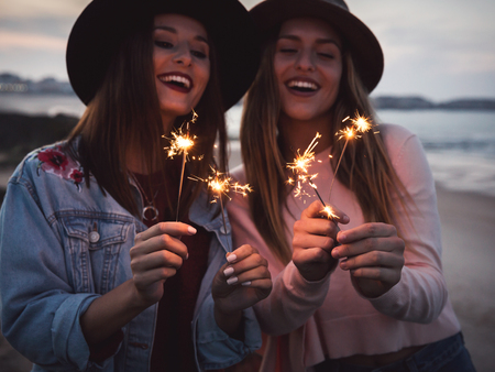 Two beautiful friends celebrating holding sparklers at beachの写真素材