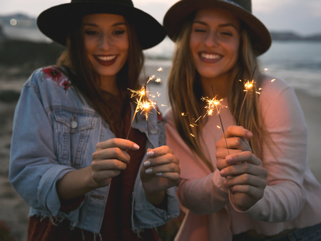 Two best friends celebrating, holding sparklers at beachの写真素材