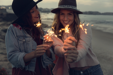 Two best friends celebrating, holding sparklers at beachの写真素材