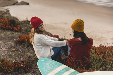 Two best friends sitting near the coastline with her surfboards while looking to the oceanの写真素材