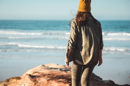 Woman with a yellow cap and walking over a cliff to see the beachの写真素材