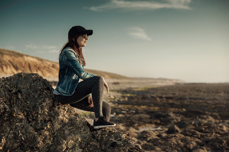 Beautiful woman alone in the beach sitting on the rocksの写真素材