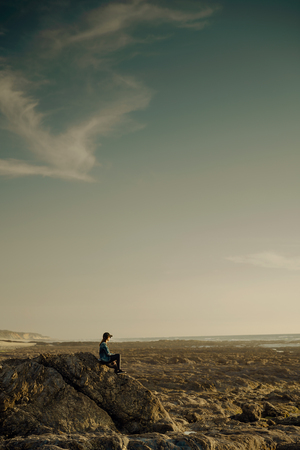 Beautiful woman alone in the beach sitting on the rocksの写真素材