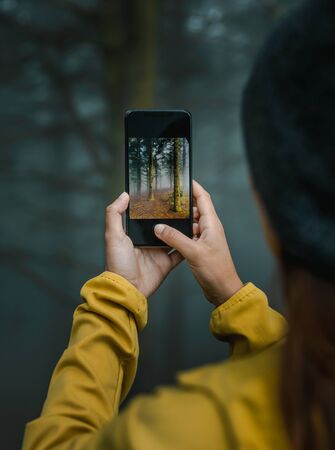 Female traveler taking a picture to a forest with her cellphoneの写真素材