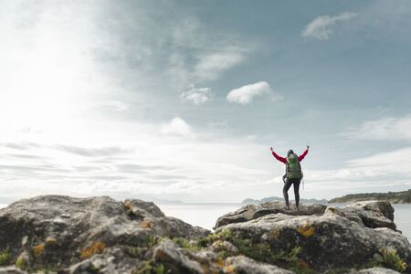 Woman with backpack and arms raised  enjoying the beautiful view of the coast