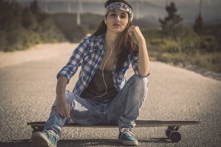 Beautiful young skateboarder girl sitting over her skateの写真素材
