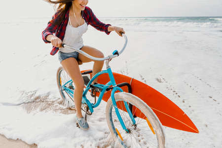 Surfer young woman riding her bicycle on the beachの写真素材