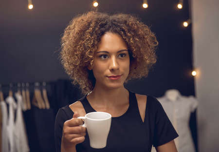 Young fashion designer on her atelier making a pause and drinking coffeeの写真素材