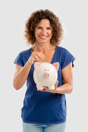 Portrait of a happy middle aged woman puting some money on a Piggybankの写真素材