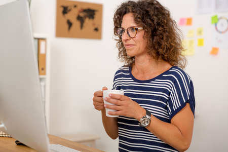 Middle aged woman working on the office and drinking coffeeの写真素材
