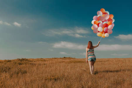 Beautiful young woman walking on meadow holding ballons