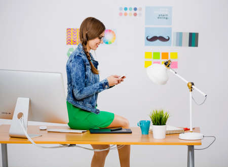 Woman working at desk In a creative office and texting a messageの写真素材