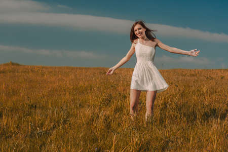 Young beautiful woman walking on a meadow wearing a white dress