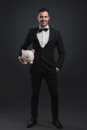 Man in tuxedo holding a pig money boxの写真素材