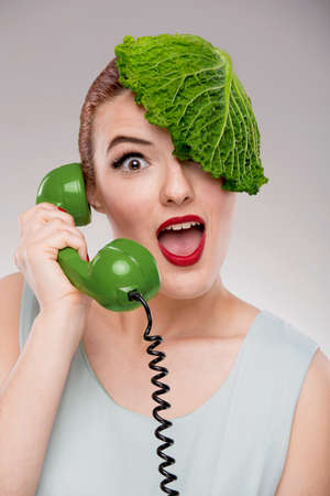 Portrait of a woman illustrating a vegan concept with a cabbage on the head and making a ecological green callの写真素材