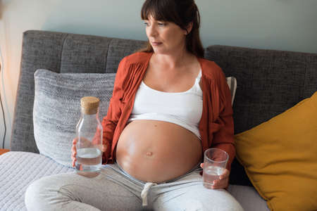 Pregnant woman holding glass of water relaxing in bed at homeの写真素材