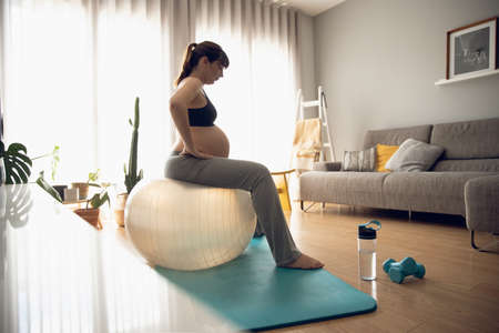Pregnant woman working out at home doing exercises on a fitball. Keeping in good shape while waiting for babyの写真素材