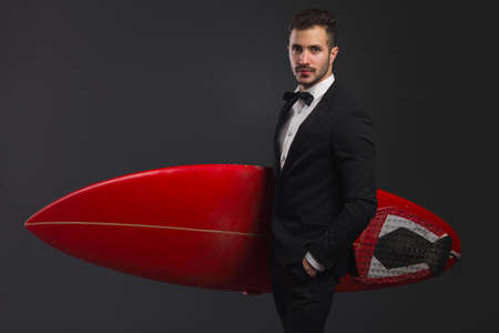 Studio portrait of a fashion young man wearing a suit and posing with a surfboardの写真素材
