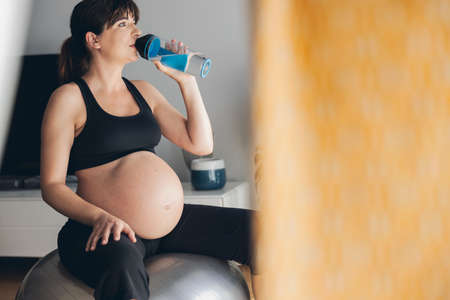 Pregnant woman drjinking water after her working out at home. Keeping in shape while waiting for the babyの写真素材