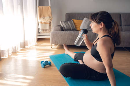 Pregnant woman drjinking water after her working out at home. Keeping in shape while waiting for the babyの写真素材
