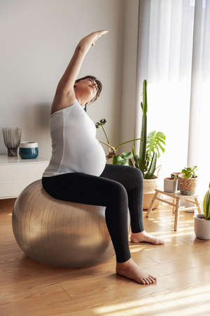 Pregnant woman working out at home doing stretching exercises. Keeping in good shape while waiting for babyの写真素材