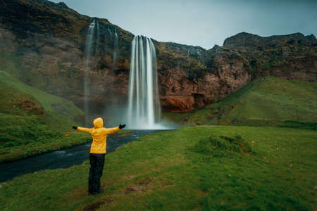 Woman in yellow with arms raised on the Seljalandsfoss waterfall, Icelandの写真素材