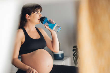 Pregnant woman drjinking water after her working out at home. Keeping in shape while waiting for the babyの写真素材