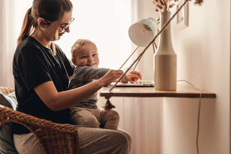 Busy woman working at home with a baby in the lapの写真素材