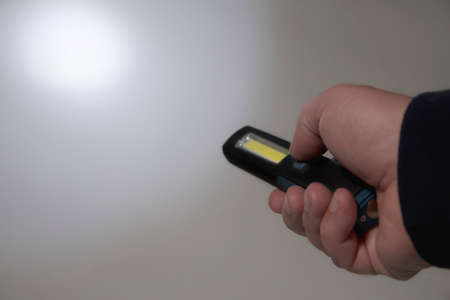 Pocket led flashlight in hand. illuminates gray background. Copy space. Circle of lightの写真素材