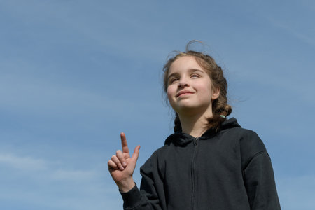Spring mood. Teenage girl smiling against the background of the spring sky. A finger pointing upの写真素材