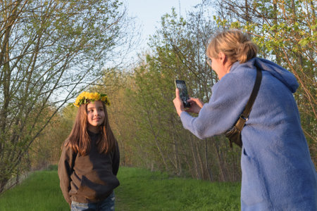 Family photography at sunset in the forest. Mom takes a picture of her daughter on a smartphone in natureの写真素材