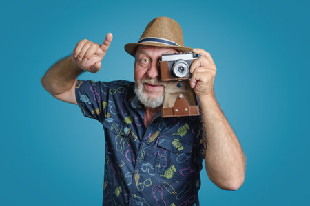 Say Cheese taking picture. Happy senior man gray beard and straw hat with retro camera. Rising finger portrait. Blue background.の写真素材