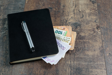 Euro banknotes and fountain pen on wood background. Accounting black book