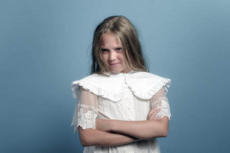 Emotions of child. Long hair angry young girl looking to the side. Arms crossed on chest. Dark blue background.の写真素材