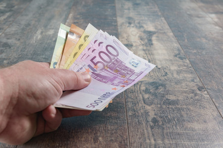 Amount of large banknotes euro money in the male hand. Wooden texture rustic background close-up