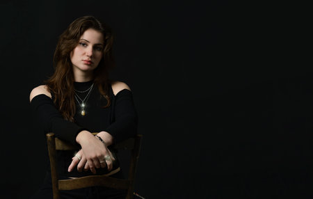 Beautiful tender girl in a black top with beautiful long dark hair.Elegant pose on a chair. Black...