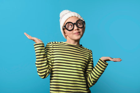 shy girl in a yellow striped tank top and winter hat, looking away, blue background