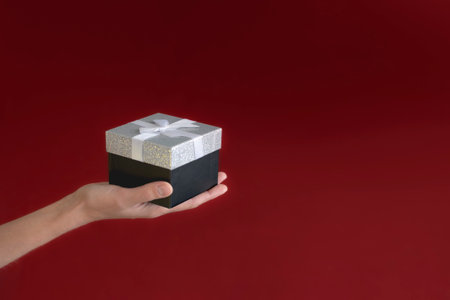 Woman holding a gift box. Dark - Burgundy background, copy space bannerの写真素材