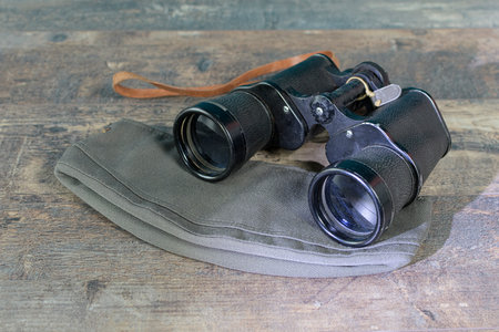 Old military binoculars with traces of time and dust lying on a wooden table.の写真素材
