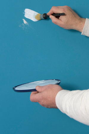 Test of color and quality of paint. a brush in a man's hand and smears of light blue paint on a dark blue wallの写真素材