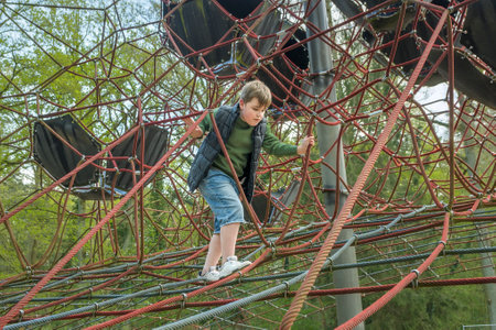 Teenage boy climbing on spider web with expression in public park. Spring sunny dayの写真素材