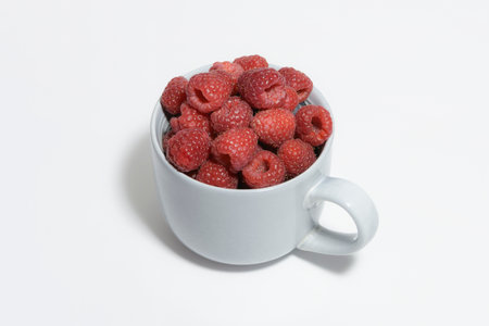 Large gray mug filled to the brim with fresh raspberries on a white backgroundの写真素材