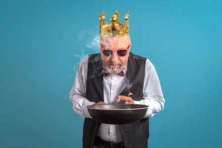 King of kitchen. A man in gold corona with a burnt frying pan in his hand. On a blue backgroundの写真素材