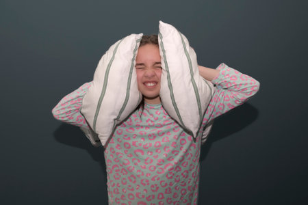 Teenage girl can't sleep. The girl covers her ears with pillows from a loud sound. Insomnia in...