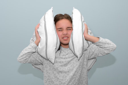 The girl covers her ears with pillows from a loud sound. Insomnia in teenagers. portrait studio....