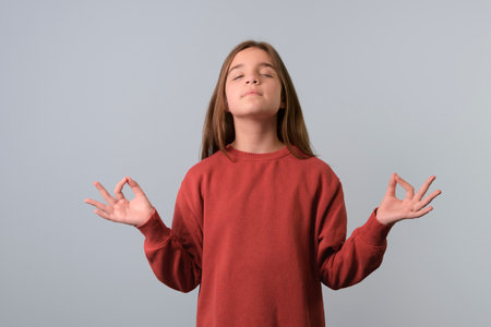 Beautiful teenager girl wearing red sweater over blue background doing yoga, keeping eyes closed, holding fingers in mudra gesture. meditationの写真素材